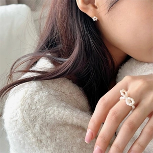 Close-up of pearl bow ring and floral earrings set on model with soft lighting