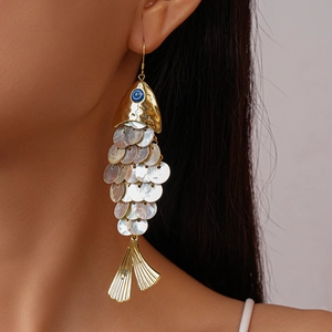 Detail view of golden fish earrings with dangling shell pieces on a female model