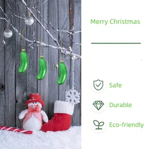 Hand-blown glass green pickle Christmas ornaments hanging on a snowy tree branch