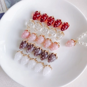 Macro detail of resin strawberry charms with pearl accents and gold metal loops