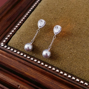 Detailed view of silver drop earrings with zircons and gray pearls on green velvet