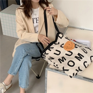 Detail der beigen Canvas-Tasche mit orangefarbenem Smiley und schwarzem Buchstabendruck