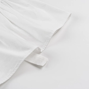 Détail de la blouse en coton blanc montrant la double couture et le ruban à nouer