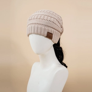 Detail of apricot cable knit ponytail beanie with faux leather tag on a studio mannequin
