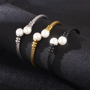 Braided steel wire bracelet with pearls in gold, silver, and black on a display stand