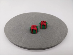 Makro-Detail von 3D-Weihnachtsgeschenk-Ohrringen in Grün mit roter Schleife auf grauem Sockel