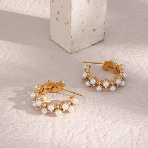 Detail of gold C-shaped earrings with inlaid white pearls and sparkling crystal stones