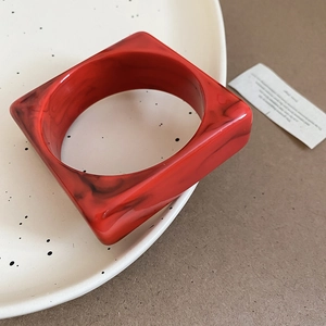 Macro detail of square red marble acrylic bangle with unique black swirl patterns