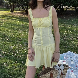 Detail of light yellow mini dress featuring button front and ruffled hem on a sunny lawn