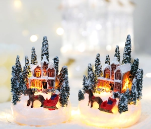 Detail of glowing LED Christmas house with red roof, snow trees and horse-drawn sleigh