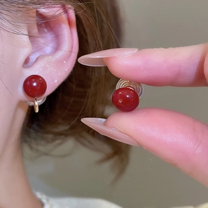 Detail of red circular clip-on earring with transparent silicone cushion on model ear