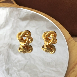 Polished gold knot earrings reflecting on a mirror surface over natural wood background