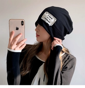 Side view of a woman wearing a black knit beanie with a stylish white square patch
