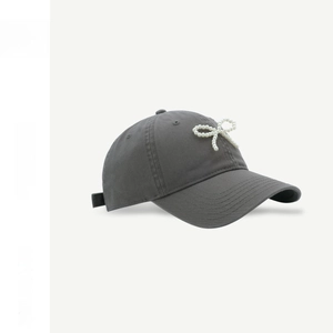 Detail of dark grey baseball cap with white pearl bow decoration and cotton twill texture