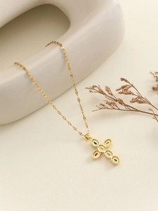 Close-up of golden cross necklace with colorful micro-inlaid zircon stones on a soft background