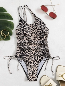 Flat lay of leopard print one-piece swimsuit with drawstring details and summer accessories