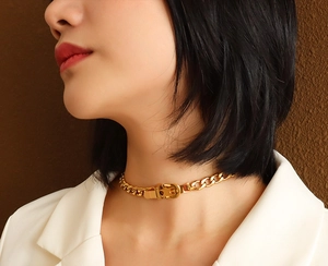 Close-up of golden belt-buckle style thick chain necklace worn by a model in white suit