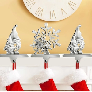 Silver metal Christmas stocking hooks with gnome and snowflake designs on white mantel