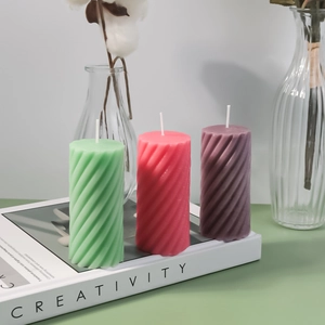Detailed view of spiral pillar candles in mint green, coral pink, and deep purple colors