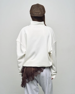 Rear view of a white oversized zip collar sweatshirt styled with a brown newsboy cap