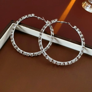 Detailed close-up of large silver hoop earrings with clear rhinestones on a tray