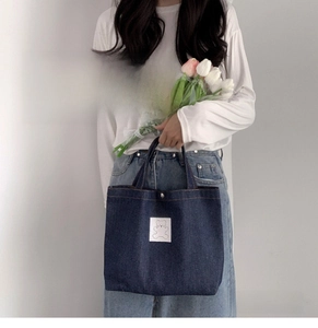 Detail of blue denim tote bag with white bear patch held by model in casual setting