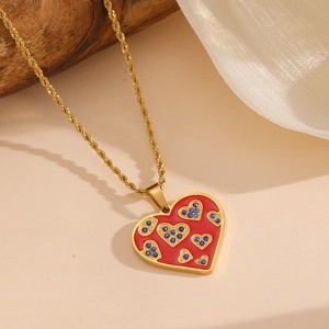 Collier chaîne dorée avec pendentif cœur rouge et strass bleus sur fond beige naturel