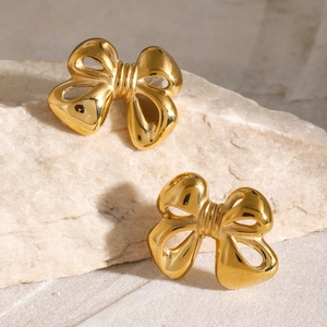 Macro shot of 18k gold plated bow stud earrings on a natural white marble background