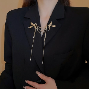 Dettaglio della spilla a fenice dorata con perle e nappe su una giacca nera elegante