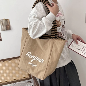 Detail of khaki tote bag with plush striped strap and Bonjour magic lettering