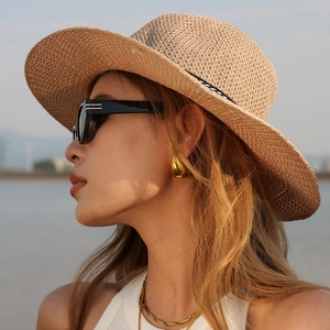 Close-up of golden teardrop earrings worn with a straw hat and sunglasses outdoors