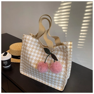 Close-up of beige houndstooth canvas tote bag with a pink cherry charm and shadow detail