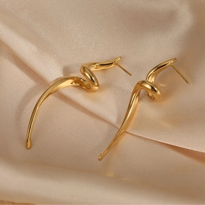 Close-up of golden twisted spiral earrings on soft beige silk fabric showing metal texture
