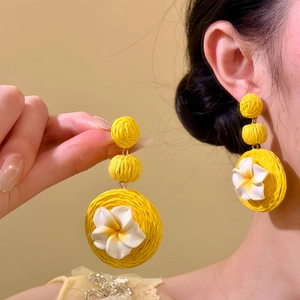 Primo piano di orecchini in rafia gialla con fiori in argilla bianca in stile tropicale