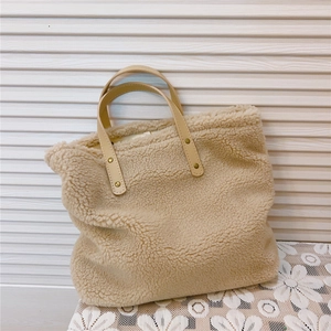Detailed shot of beige lamb wool tote bag featuring brown leather handles and gold rivets