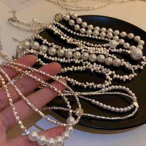 Detail of layered silver metal necklace featuring white pearls on a black background