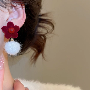 Close-up of red velvet flower earrings with white fur pompom on model's ear