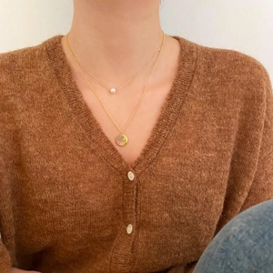 Close-up of a double-layered gold necklace with a pearl and moon charm worn by a model
