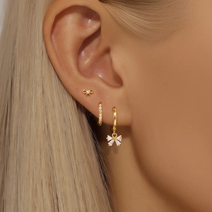 Close-up of gold bow earrings and zircon hoop set worn on a model's ear