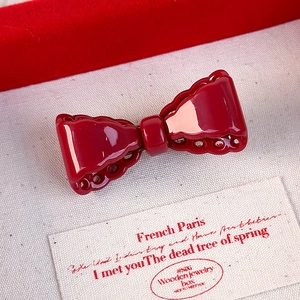 Close-up of vintage red bow hair clip with intricate hollowed edges and glossy finish