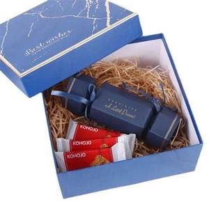 Detail of square navy blue gift box with marble lid, gold accents and raffia filling