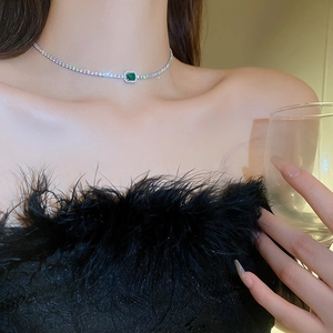 Detail of emerald cut zircon choker necklace worn by model against black feathers