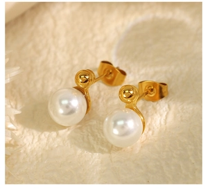 Close-up of elegant gold pearl earrings with two round white pearls on textured background