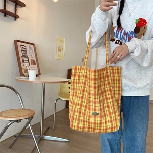 Close-up of a large yellow plaid canvas tote bag with a detailed oval metal brand tag