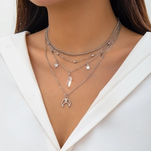 Close-up of layered silver chain necklace with star, crystal, and crescent moon pendants