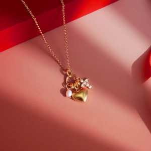 Detail von goldenem Herz, weißer Perle und Kreuzanhänger mit Strass an einer Halskette