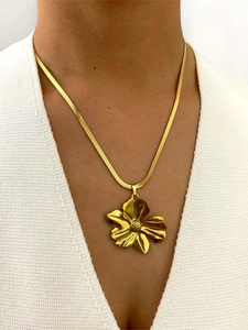Macro view of a large golden flower pendant on a flat snake chain worn by a model