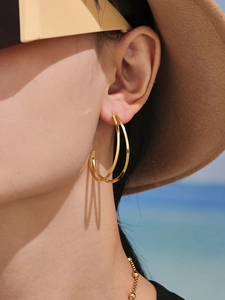 Gros plan de boucles d'oreilles doubles créoles dorées portées par un mannequin à la plage