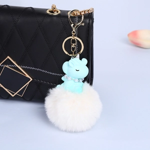 Blue resin unicorn charm with pearl necklace and white pom pom on a quilted bag