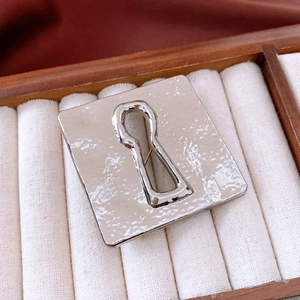 Macro shot of silver square brooch featuring a keyhole cutout and hammered metal texture